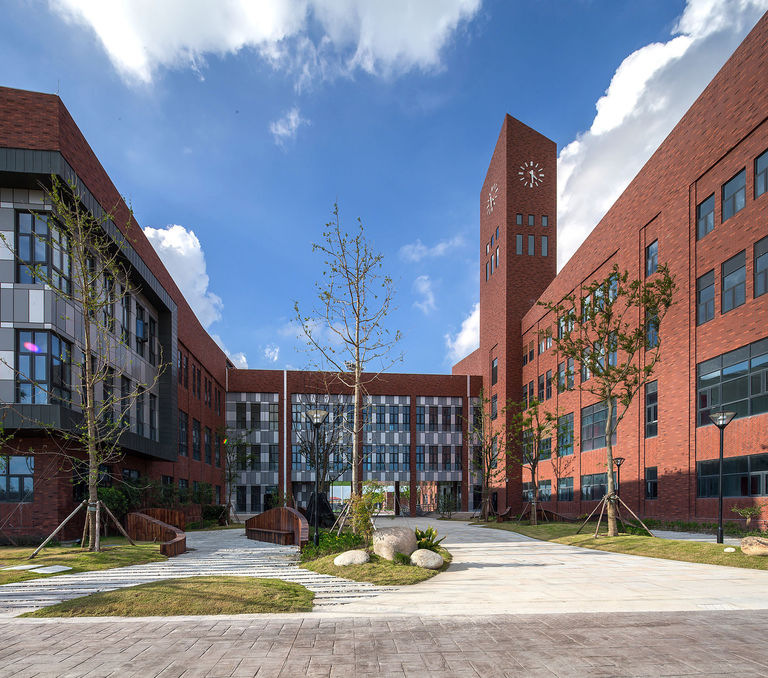 Photo of landscaped entrance square to Dulwich College Puxi in Minhang, Shanghai, featuring clocktower and red brick façade.