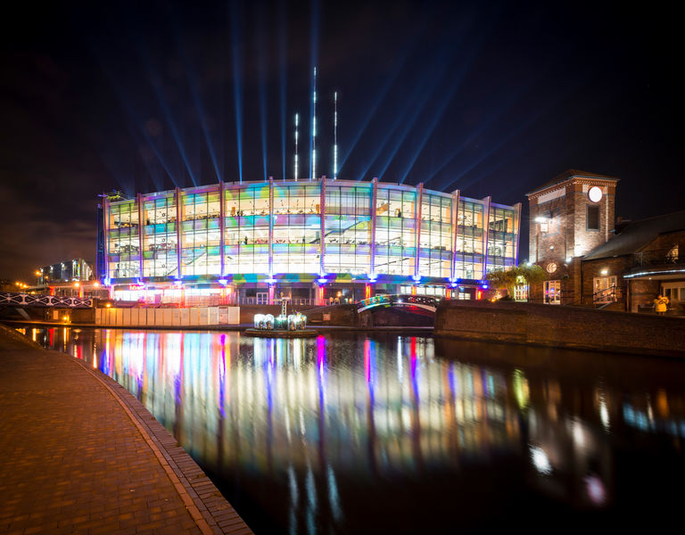 Exterior night photo of Barclaycard Arena in Birmingham, with new glass façade, LCD wonderwall and iconic Sky needles.