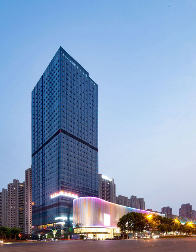 External night photo of 150 metre high office building, curved retail block and street landscaping at ID Mall in Hefei, China.